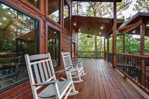 A wooden deck with rocking chairs and large windows overlooking a forest. - Sleek Cabin w/ Hot Tub: 11 Mi to Broken Bow Lake! (Broken Bow)