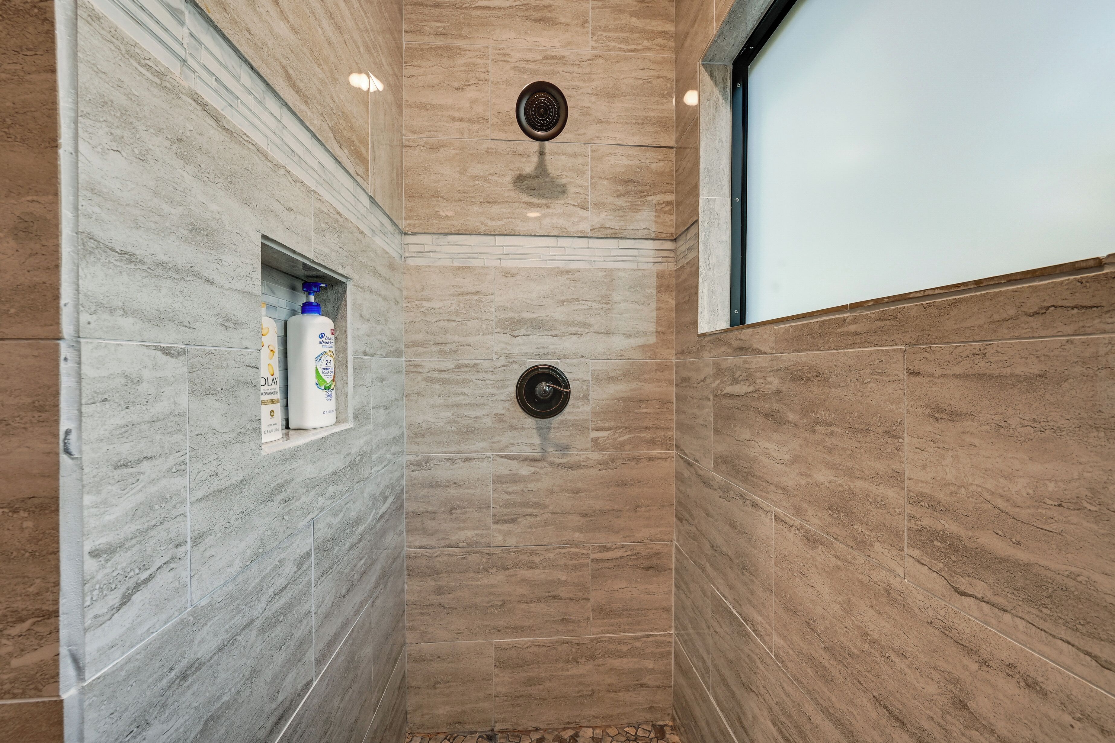 Un espace douche avec un mur en marbre, une étagère intégrée pour les articles de toilette et un drain circulaire.