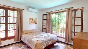 Un dormitorio con cama, ventanas amplias, cabecero de madera y aire acondicionado instalado en la pared.