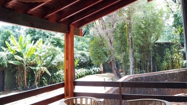 Una terraza de madera con dos sillas de madera y una pequeña mesa redonda, rodeada de exuberante follaje.