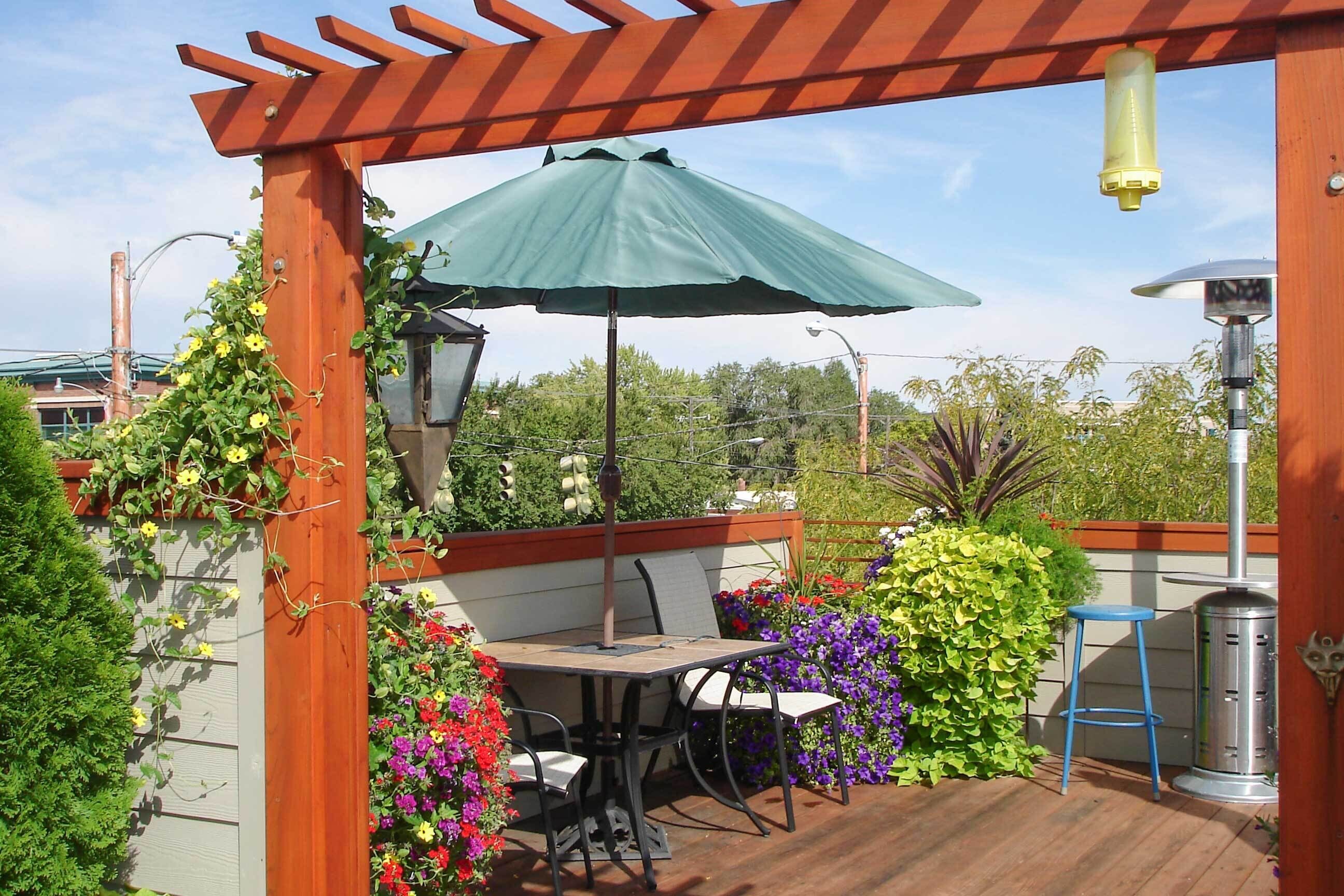A patio with a table and chairs, a green umbrella, and a metal grill.