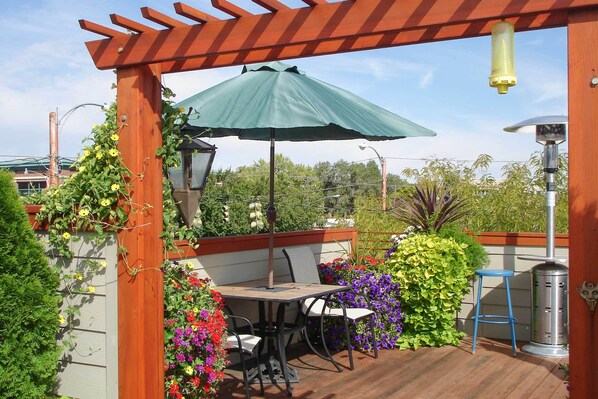 Un patio con una mesa, sillas, un paraguas verde y una parrilla de metal.