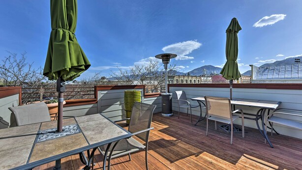An outdoor patio with a table and chairs, a trash can, and two green umbrellas. - Walkable Downtown Logan Apartment w/ Rooftop Deck (Logan)