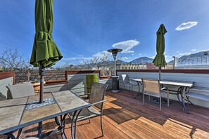 Un patio al aire libre con una mesa, sillas, un bote de basura y dos sombrillas verdes.
