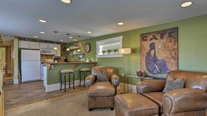 A living room with brown leather chairs and ottomans, a kitchen in the background, and a large 'CAFE' painting on the wall. - Walkable Downtown Logan Apartment w/ Rooftop Deck (Logan)
