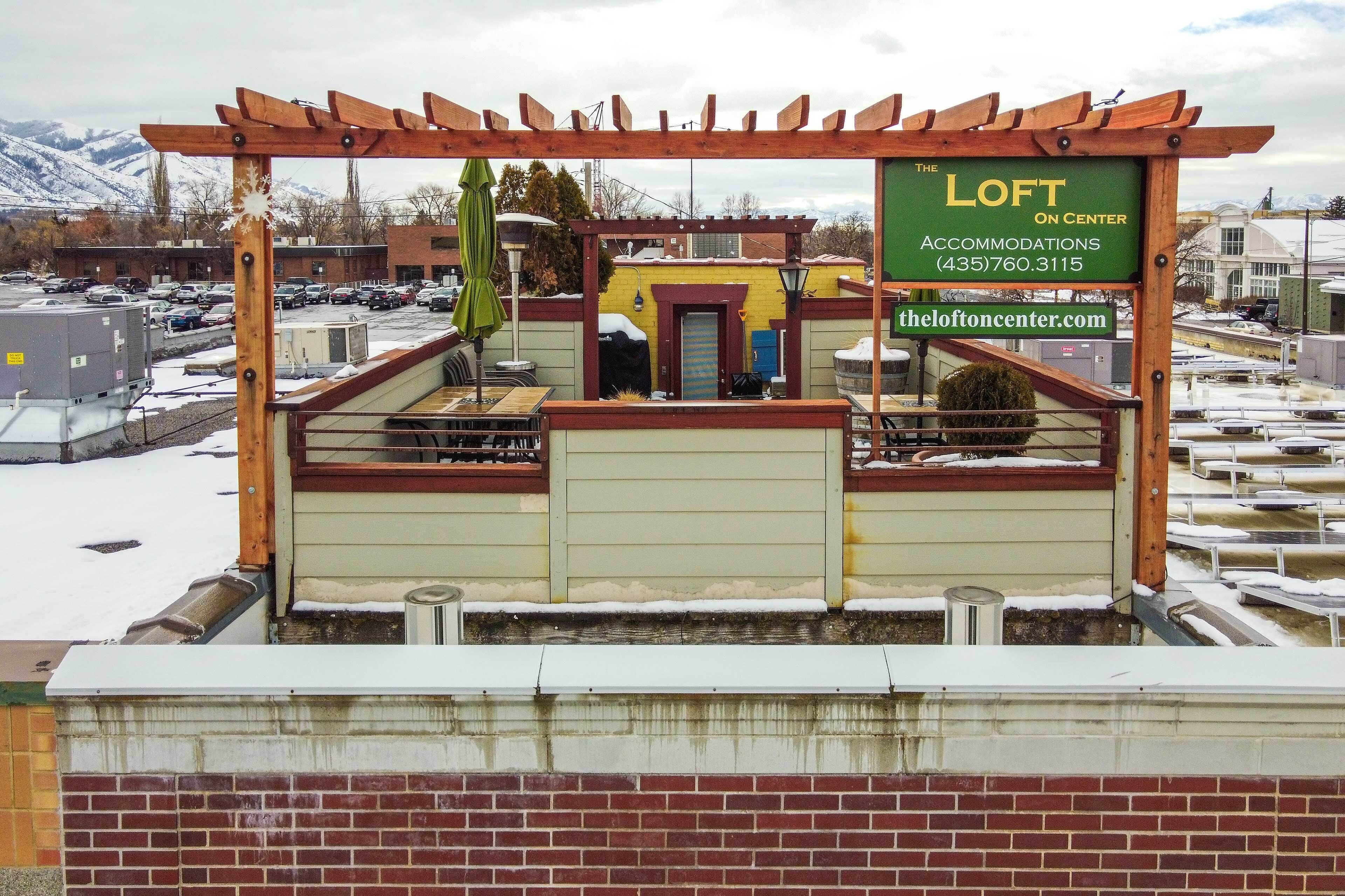 Un patio en la azotea con un pergolado de madera, un letrero que dice 'The Loft on Center' y vistas de un estacionamiento y edificios al fondo.