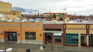 A building with a brick facade, a sign for a loft, and a view of snow-covered mountains in the background. - Walkable Downtown Logan Apartment w/ Rooftop Deck (Logan)