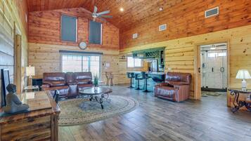 A spacious living room with leather furniture, a wooden ceiling, and a large window.