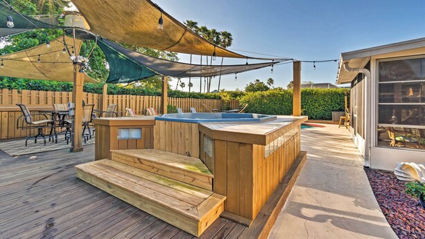 Een houten terras met een jacuzzi, buitenmeubels en een overdekt gebied met lichtjes.