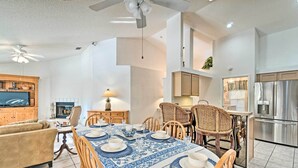Een ruime woonkamer met een grote televisie, een eetgedeelte met blauwe tafelkleden, houten stoelen en een keuken met roestvrijstalen apparatuur.