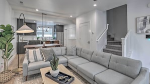 A modern living room with a grey sectional sofa, a coffee table, and a dining area in the background. - Chic & Sunny Provo Townhome w/ Rooftop Deck! (Provo)