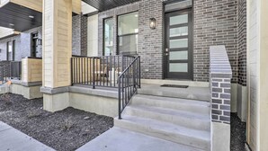 A building with a brick facade, a black door, and a small porch with steps and a railing. - Chic & Sunny Provo Townhome w/ Rooftop Deck! (Provo)