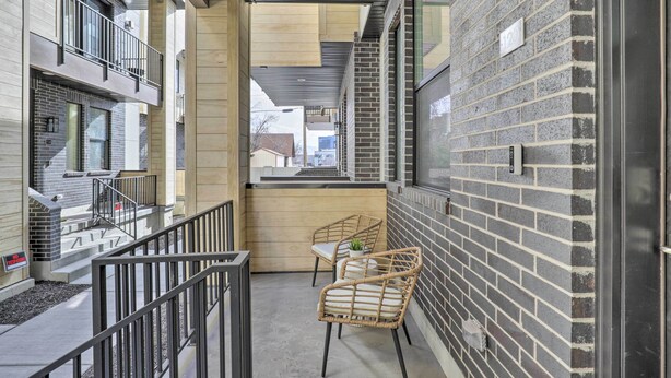 A modern building with a balcony, two wicker chairs, and a brick wall. - Chic & Sunny Provo Townhome w/ Rooftop Deck! (Provo)