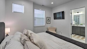 A bedroom with a bed, two windows, a ceiling fan, a TV, and a bathroom visible through an open door. - Chic & Sunny Provo Townhome w/ Rooftop Deck! (Provo)