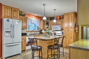 A kitchen with wooden cabinets, a refrigerator, a microwave, a coffee maker, and a sink. There are three bar stools around a central island. - Lakefront Family Getaway w/ Private Deck & Dock! (Conover)