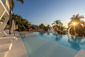 A poolside area with lounge chairs and umbrellas, surrounded by palm trees and buildings. - Puerto Vallarta Resort Condo, On-site Beach Access (Puerto Vallarta)