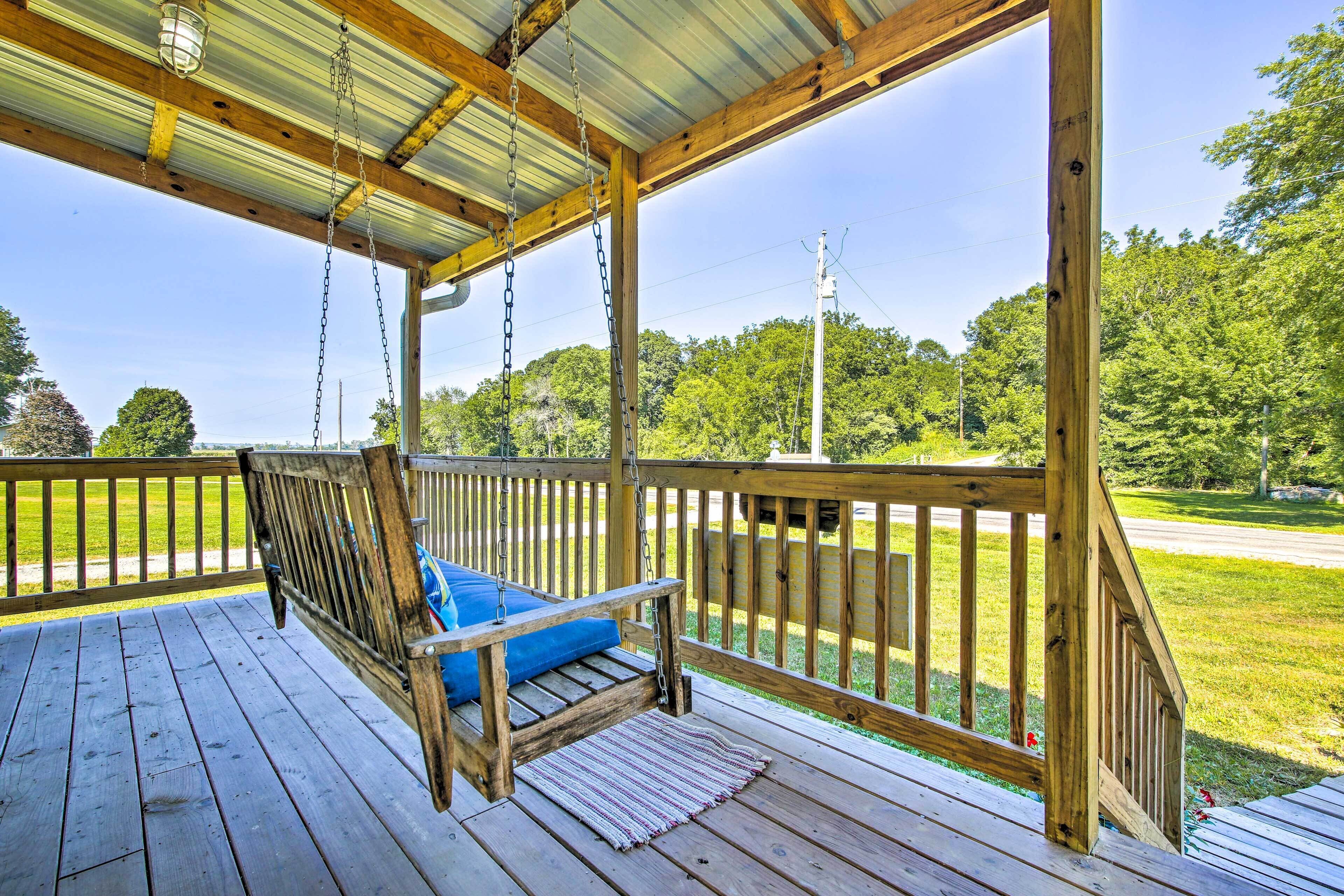 A wooden deck with a swing chair and a view of a green landscape.