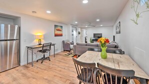 A modern kitchen with a refrigerator, a dining table with chairs, a sofa, and a TV in the living area. - Denver Area Duplex w/ Patio: Walk to Park! (Arvada)