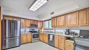 Une cuisine moderne dotée de meubles en bois, d’appareils électroménagers en acier inoxydable, de plans de travail en granit et d’une fenêtre laissant entrer la lumière naturelle.