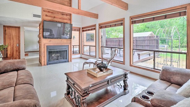 Un salon spacieux doté d’une cheminée, de poutres en bois, de grandes fenêtres et d’un coin salon confortable.