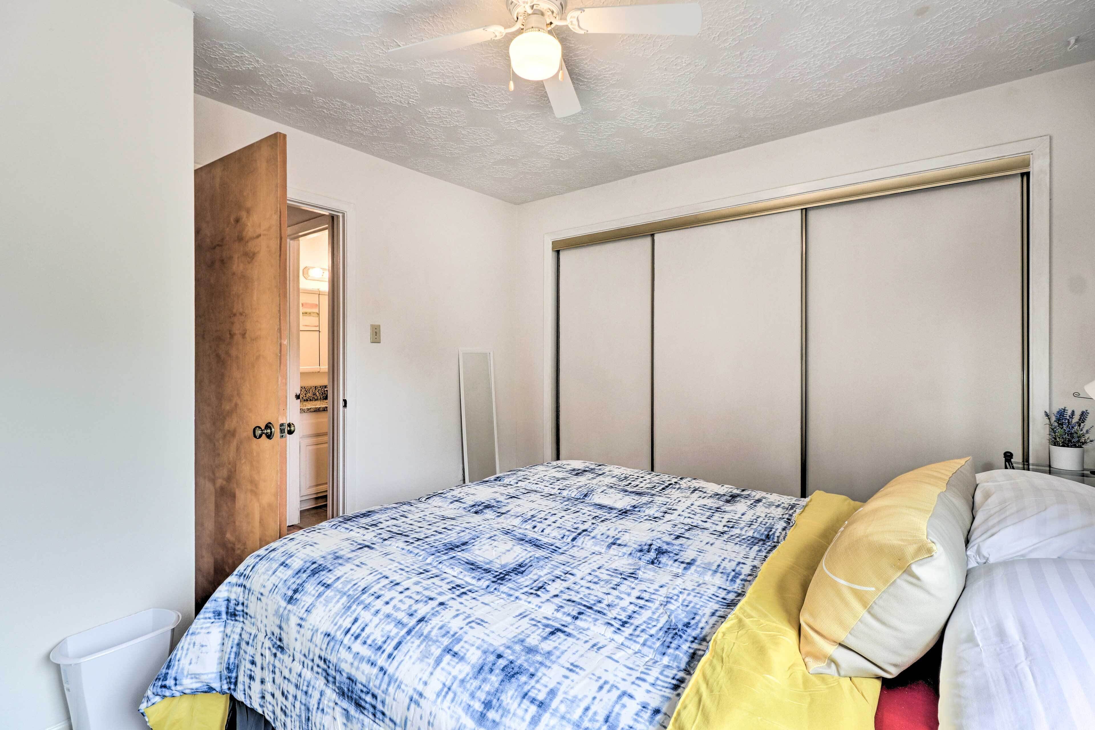 Un dormitorio con cama, ventilador de techo, armario y puerta que da a otra habitación.