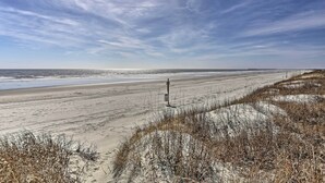 A beach with a pier extending into the water, sandy dunes, and sparse vegetation.