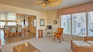 A spacious living room with a large window, a dining area, and a kitchen in the background.