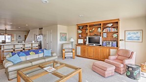 A living room with a sofa, armchairs, ottomans, a coffee table, a TV, and a bookshelf.
