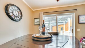 A dining table with a wine bottle and glasses, a clock on the wall, and a view of buildings through a window. - Serene Presque Isle Harbor Home on Sunrise Side! (Presque Isle)