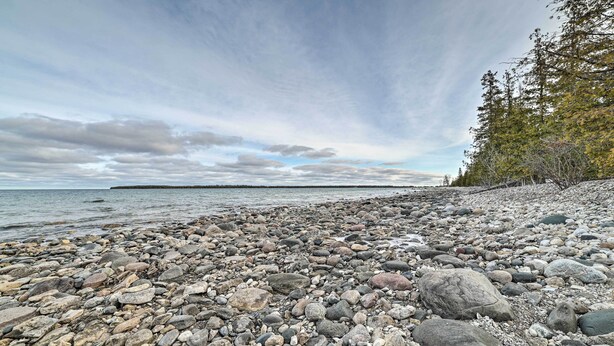 A rocky shoreline with a view of the water and trees in the background. - Serene Presque Isle Harbor Home on Sunrise Side! (Presque Isle)