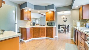 A modern kitchen with wooden cabinets, a central island, and a dining area with a chandelier. - Serene Presque Isle Harbor Home on Sunrise Side! (Presque Isle)
