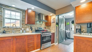 A modern kitchen with wooden cabinets, a stainless steel range hood, a built-in oven, and a dishwasher. - Serene Presque Isle Harbor Home on Sunrise Side! (Presque Isle)
