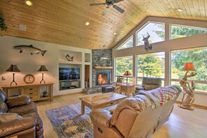 A spacious living room with a fireplace, leather sofas, and large windows offering a view of the outdoors. - Serene South Bend Family Escape; Dogs Welcome (South Bend)