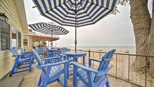 Un espacio de estar al aire libre cubierto con sillas Adirondack azules y sombrillas a rayas, con vistas a una playa.