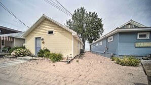 Una casa de dos pisos con fachada azul y detalles amarillos. Hay un árbol frente a la casa y un letrero que dice "Let's Do Sunset at the Sea Side Cottage".
