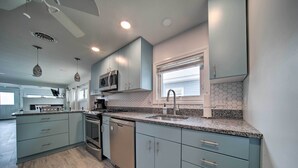 Une cuisine moderne avec des meubles de couleur bleu clair, un plan de travail en granit, des appareils électroménagers en acier inoxydable et une fenêtre équipée de stores.
