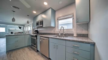 A modern kitchen with light blue cabinets, a granite countertop, stainless steel appliances, and a window with blinds.