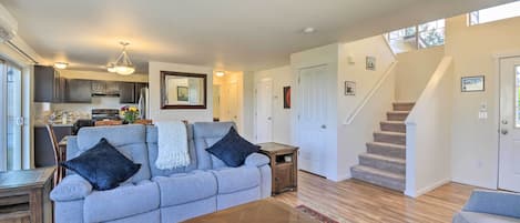 A spacious living room with a grey sofa, a wooden coffee table, and a patterned rug. A staircase leads to a second floor.