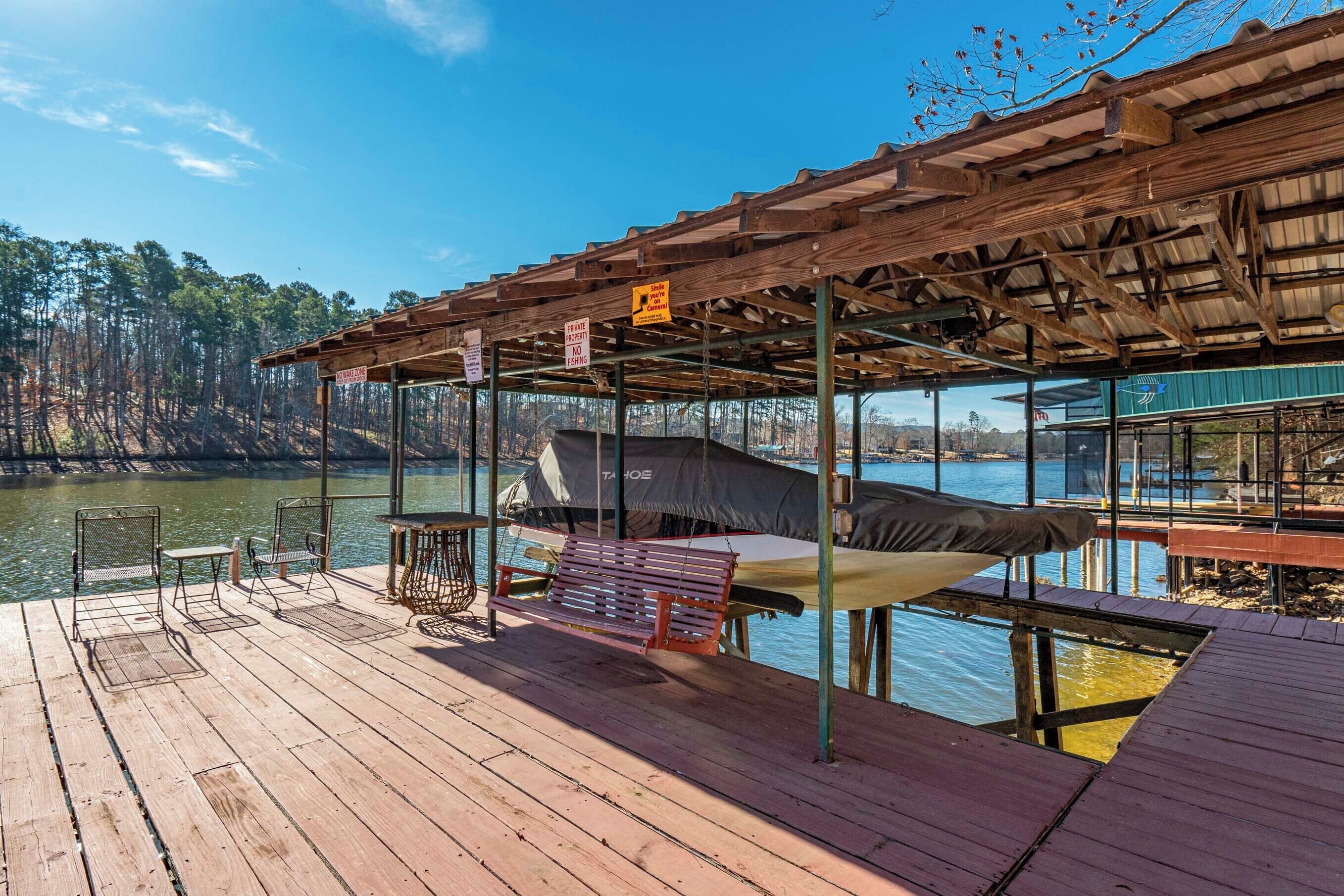 A wooden dock with a covered seating area, a grill, and a view of the water and trees.