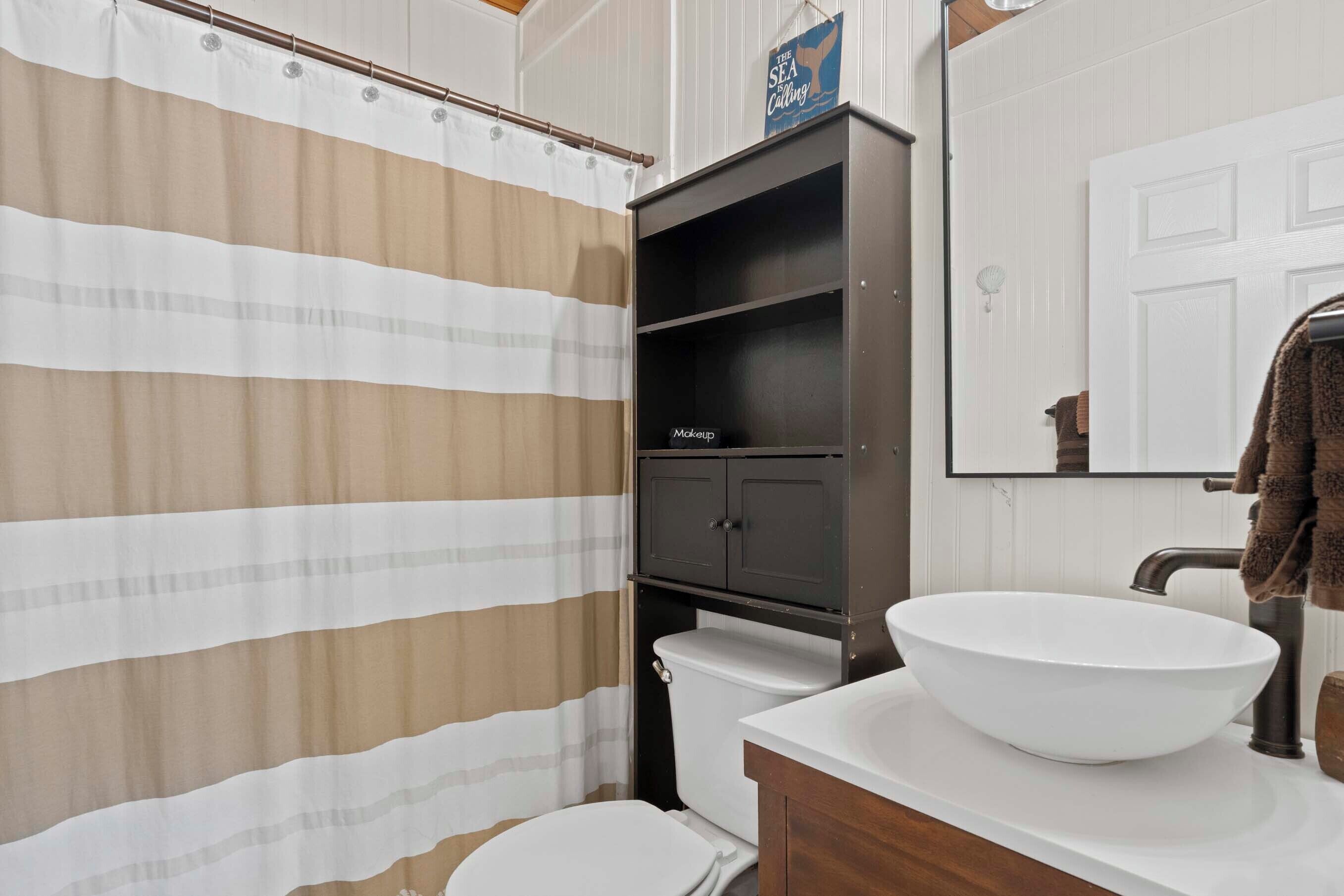 A bathroom with a striped shower curtain, a white sink with a large bowl, a dark cabinet, and a mirror above the sink.