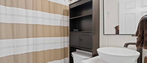 A bathroom with a striped shower curtain, a white sink with a large bowl, a dark cabinet, and a mirror above the sink.