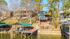 A lakeside property with docked boats, a wooden deck, and a building with a green roof. - Lakefront Home w/ Dock: 10 Mi to Central Ave! (Hot Springs)