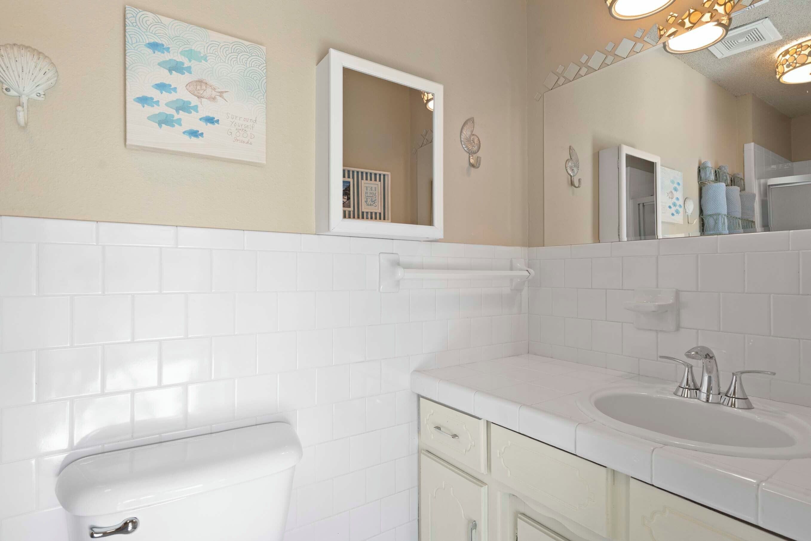 Une salle de bain avec des carreaux blancs, des toilettes, un lavabo et un miroir.