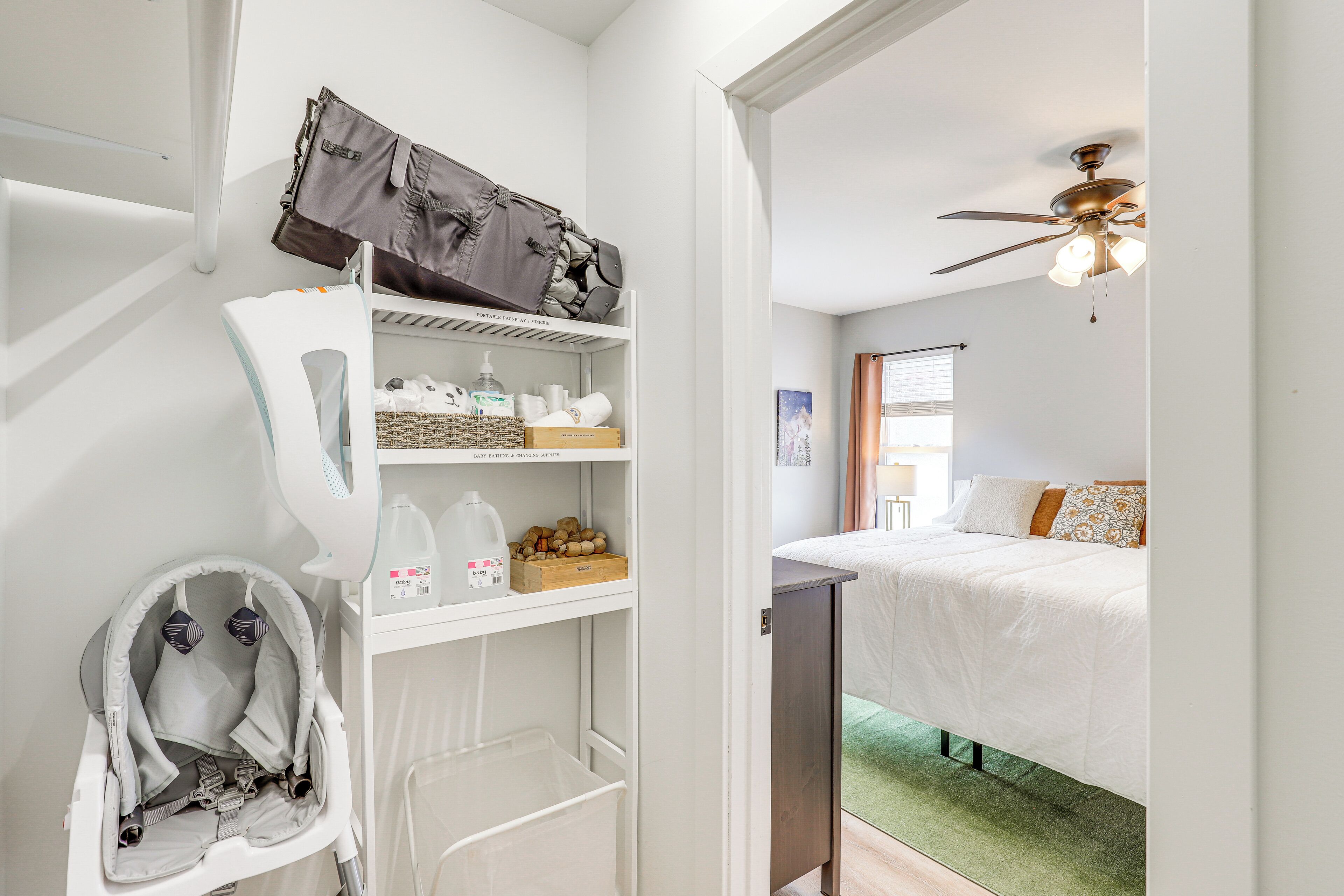 A bedroom with a bed, a ceiling fan, a desk, and a storage unit with baby items.