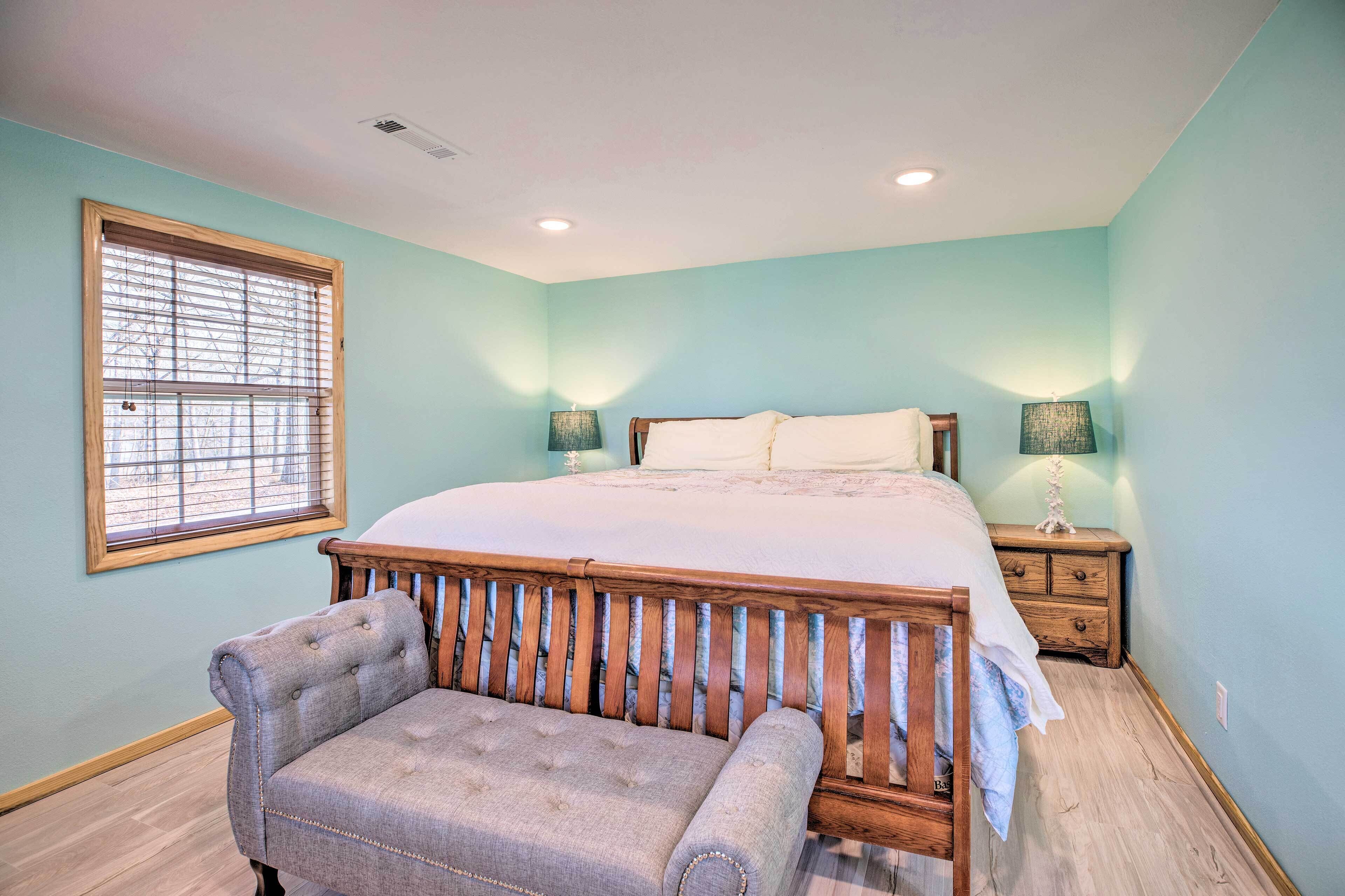 A bedroom with a bed, nightstands, a bench, and a window with blinds.
