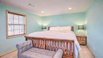 A bedroom with a bed, nightstands, a bench, and a window with blinds.
