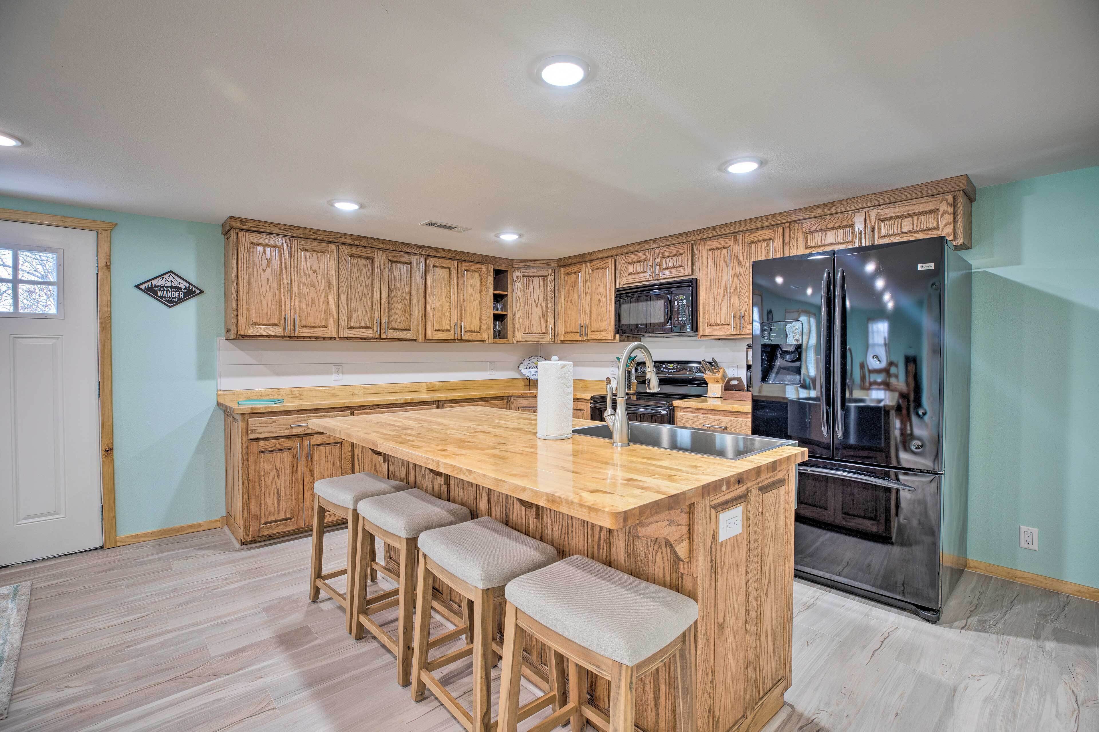 A kitchen with wooden cabinets, a stainless steel refrigerator, a microwave, and a bar stool area.