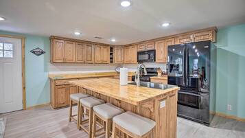 A kitchen with wooden cabinets, a stainless steel refrigerator, a microwave, and a bar stool area.