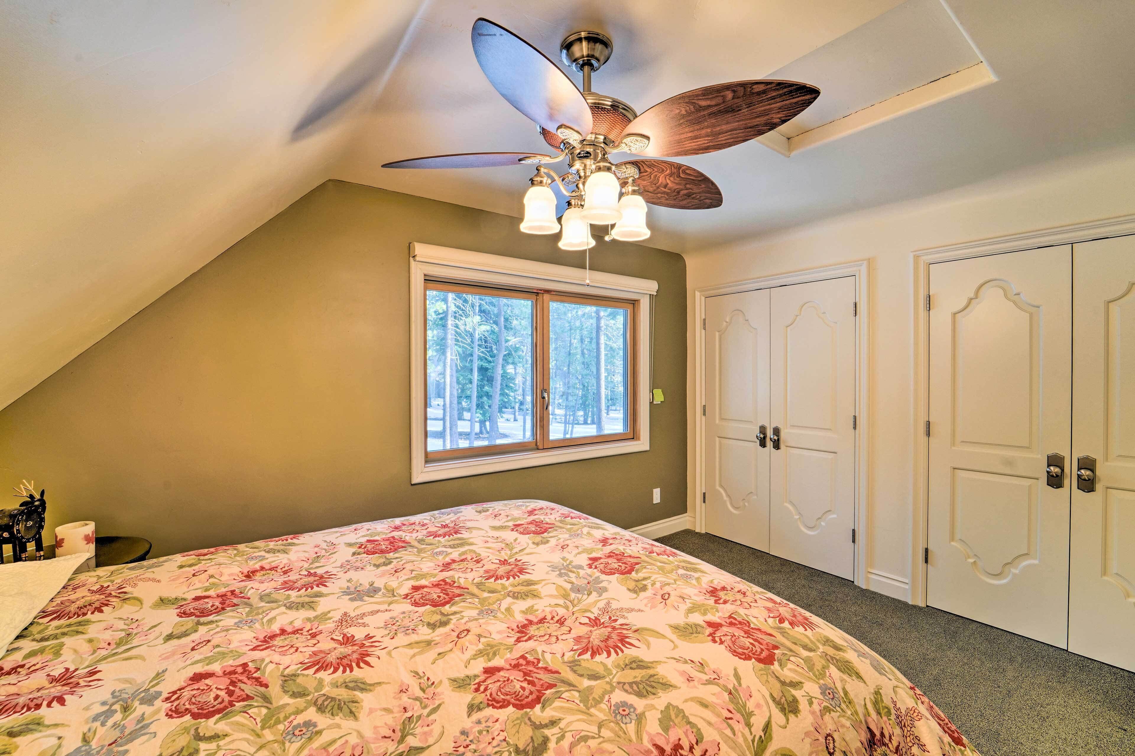 A bedroom with a ceiling fan, a large window, and a bed with floral bedding.