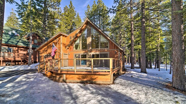 Une cabane dotée d’une grande terrasse, entourée de grands pins et avec de la neige au sol.